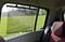 Napszemüveg-tartóval felszerelt autóablak. Kint zöld mező és fák láthatók. A roló védelmet nyújt a napsugárzás ellen.