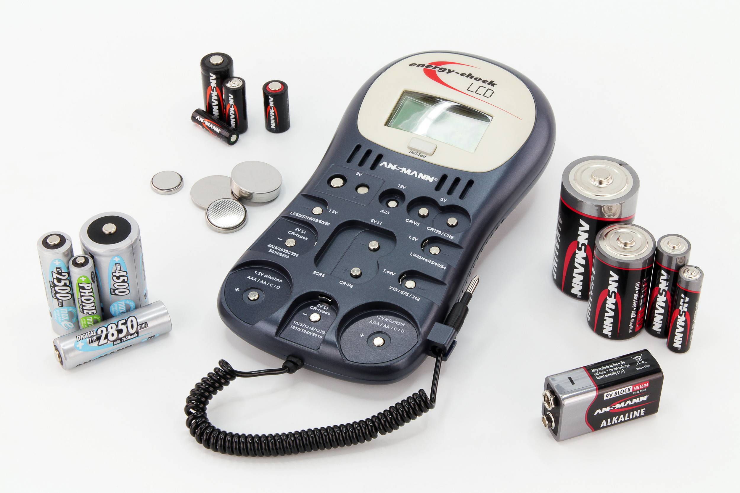 Diversi tipi di batterie sono disposti intorno a un dispositivo di test per batterie con display digitale. Mostra lo stato delle batterie.