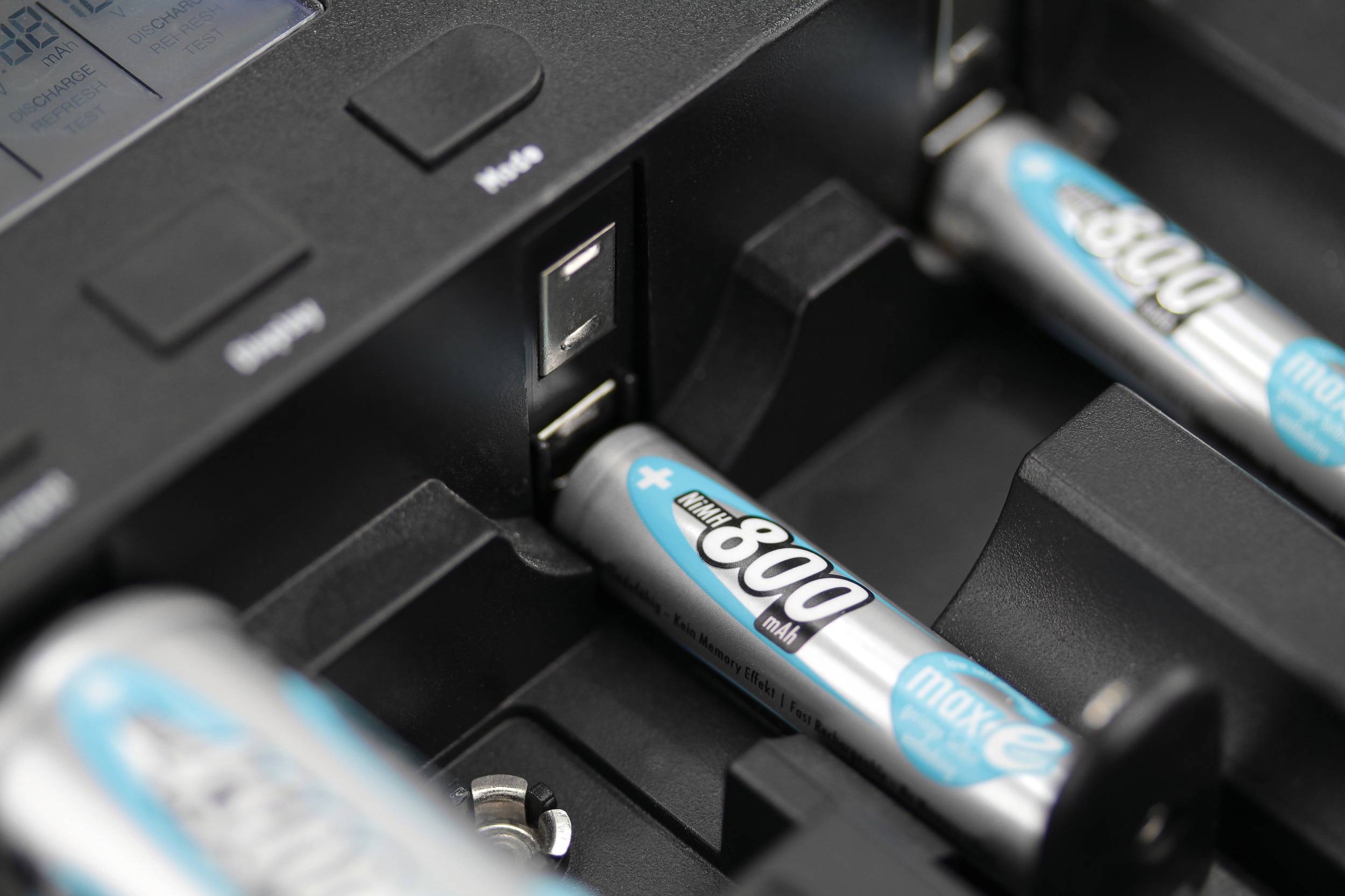 Caricabatterie con più batterie ricaricabili AA in fase di carica; focus su una batteria in uno degli alloggiamenti.