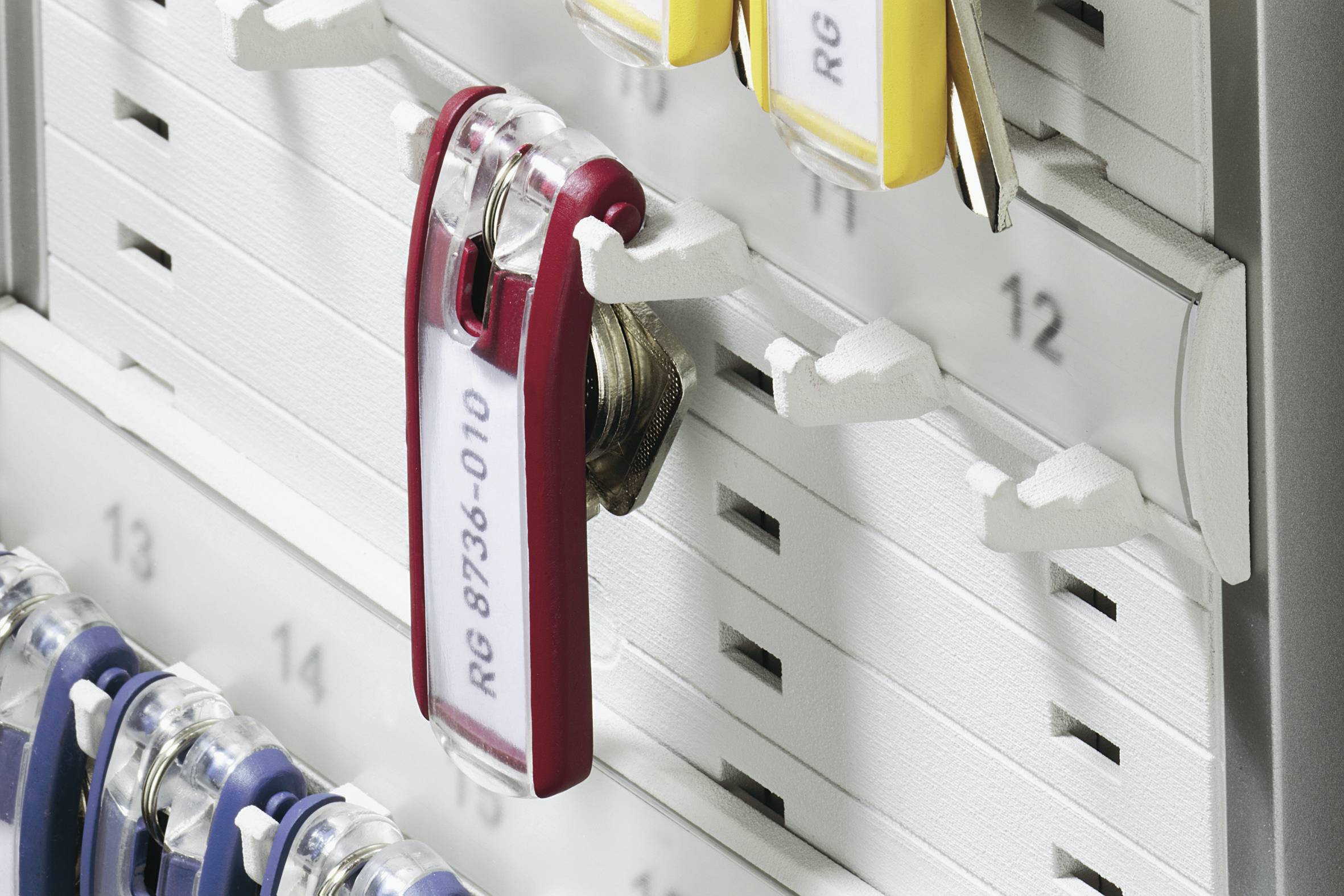 Bacheca portachiavi con ganci numerati e portachiavi etichettati. Un portachiavi rosso, contrassegnato con 'RG 8736-010', è appeso a un gancio.