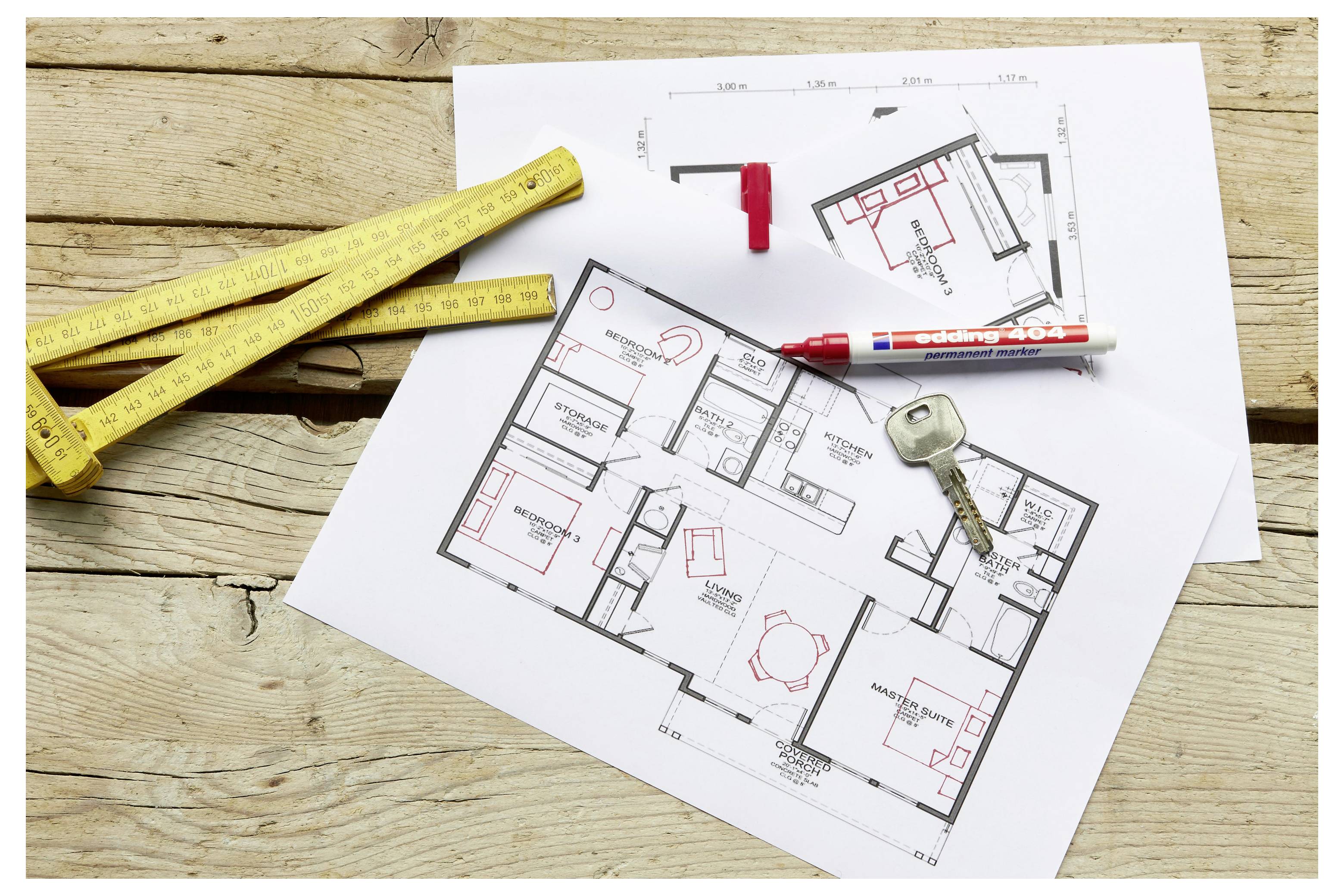 Planimetrie architettoniche su carta con un metro a nastro, un pennarello e una chiave su un tavolo di legno, che suggeriscono la ristrutturazione di una casa o la pianificazione della costruzione.