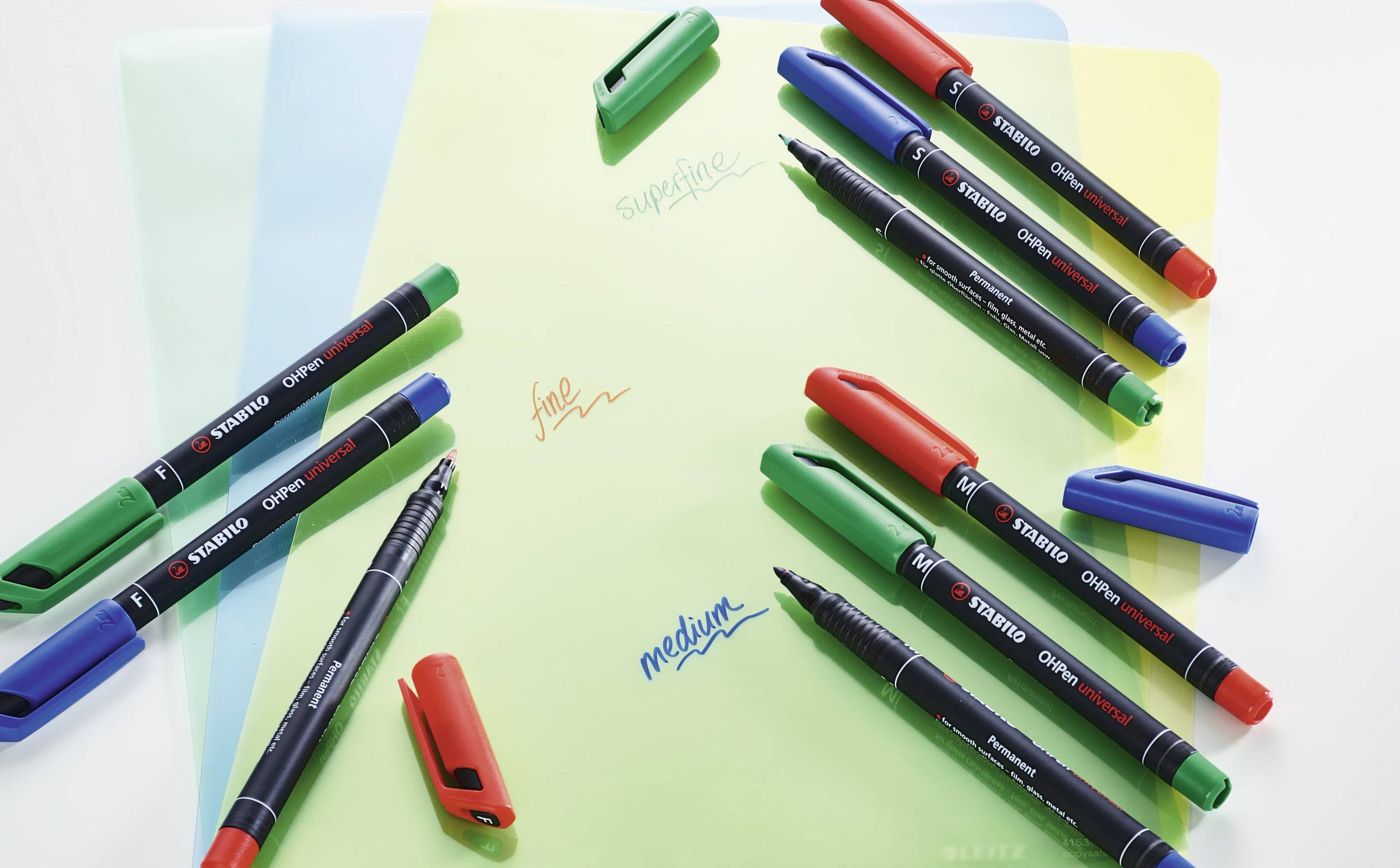 Diversi pennarelli colorati su fogli colorati, con le parole 'fine', 'medium', 'superfine' scritte, con i relativi cappucci dei pennarelli accanto.