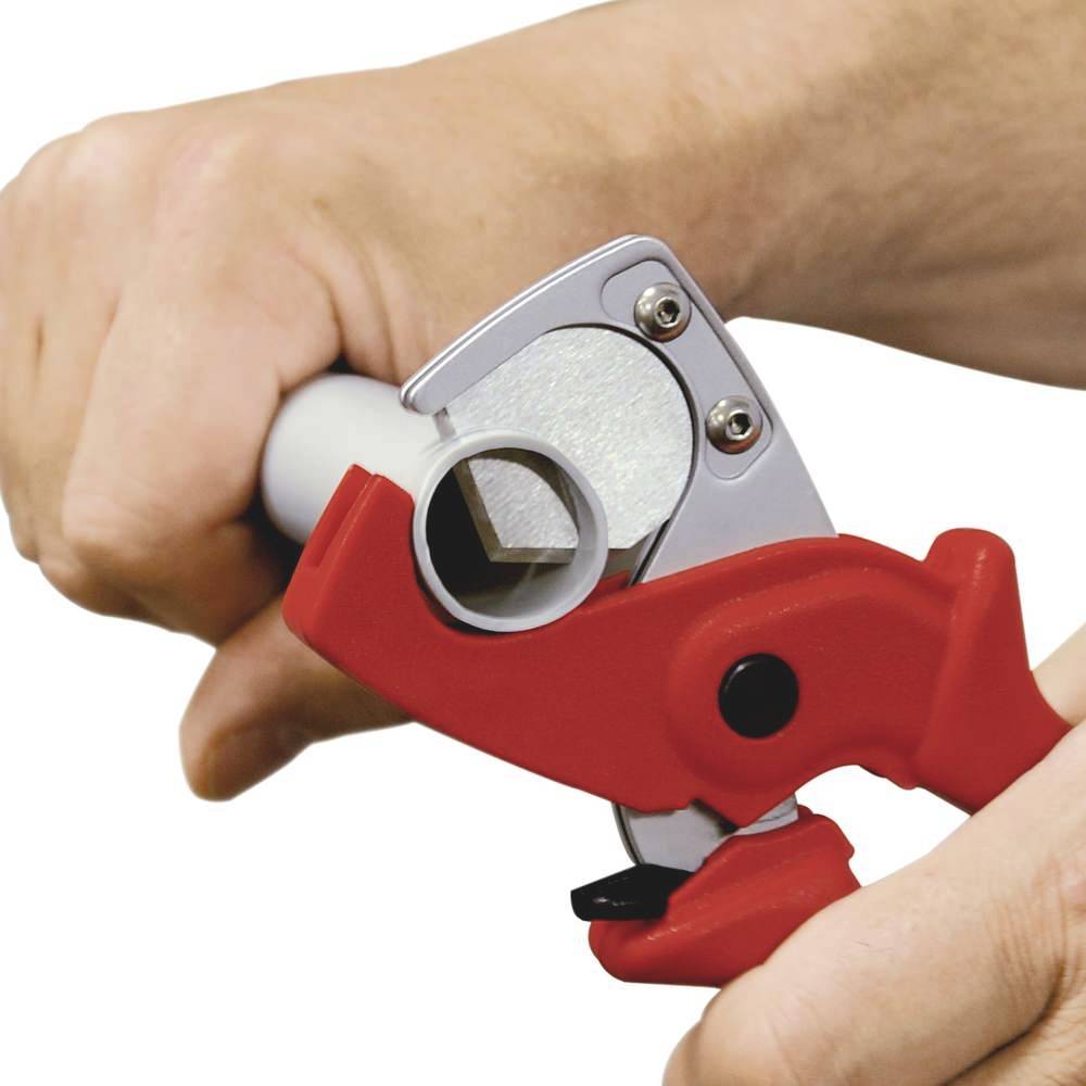Una mano taglia un tubo bianco con un tagliatubi rosso.