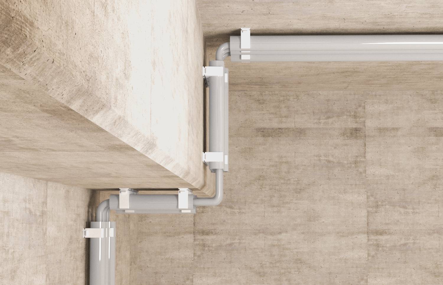 Primo piano di tubi e raccordi di condotto elettrico bianco che corrono lungo l'angolo tra il muro e il soffitto in cemento.