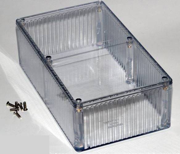 Scatola trasparente in plastica con scanalature sui lati, accanto ci sono quattro piccole viti.
