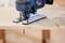 Un seghetto elettrico blu taglia con precisione una curva in una tavola di legno chiaro, mentre trucioli di legno volano tutto intorno.