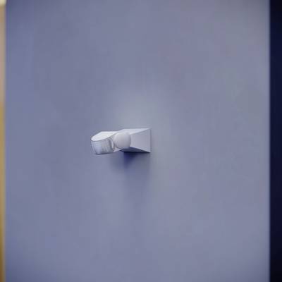 Un singolo faretto bianco illumina una parete liscia grigia.
