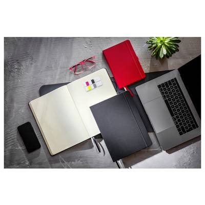 Area di lavoro alla scrivania con quaderno aperto, laptop, telefono, occhiali rossi, quaderno rosso, cartella nera, penna, foglietti adesivi e una piccola pianta.
