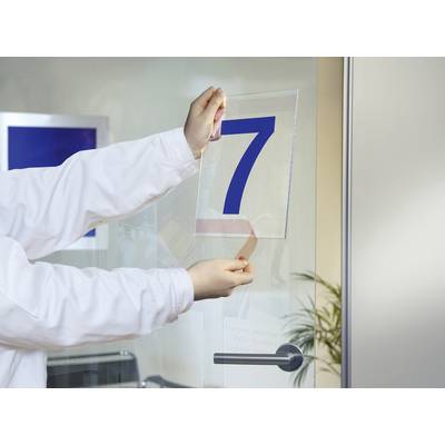 Una persona in camice bianco sta appendendo un cartello con il numero blu '7' su una porta di vetro. Sullo sfondo si intravede un ufficio.