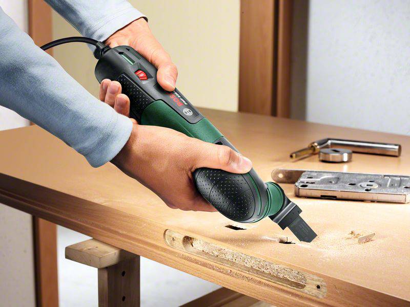 Una persona sta utilizzando un utensile elettrico multifunzione per tagliare una tavola di legno. Sono visibili residui e attrezzi.
