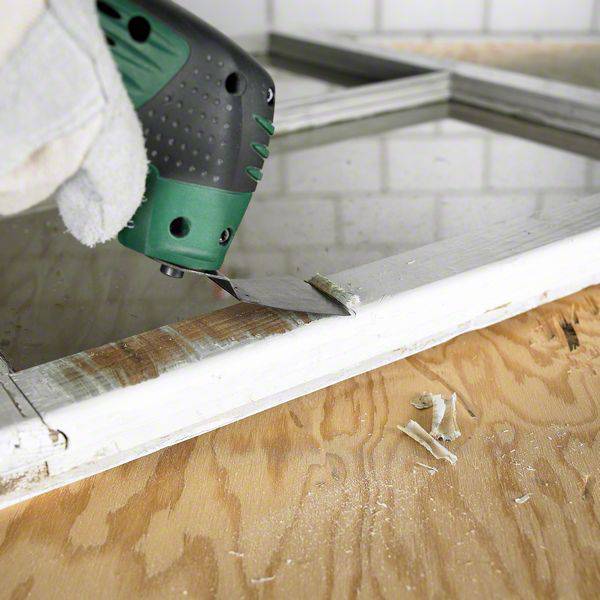 Una mano con guanti utilizza una levigatrice orbitale a batteria per levigare i bordi di una cornice in legno. Sullo sfondo sono visibili delle piastrelle.