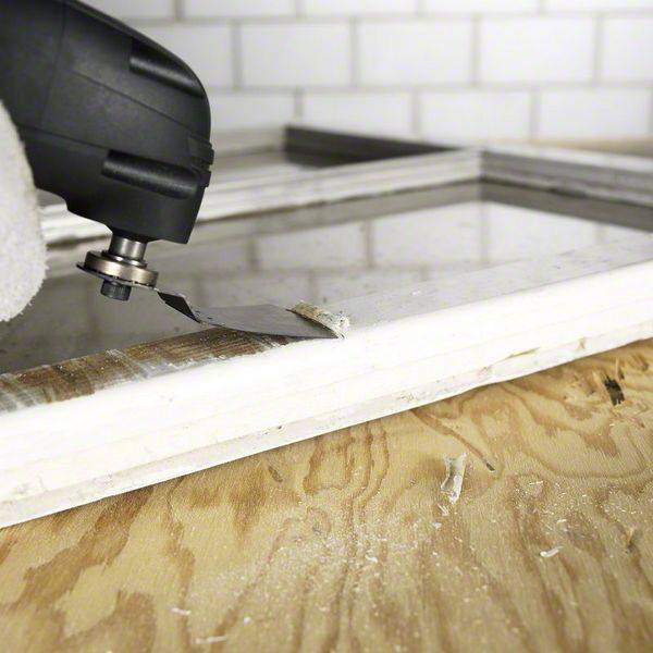 Un utensile multifunzione Dremel taglia con precisione il metallo su un tavolo di legno in un ambiente di officina.