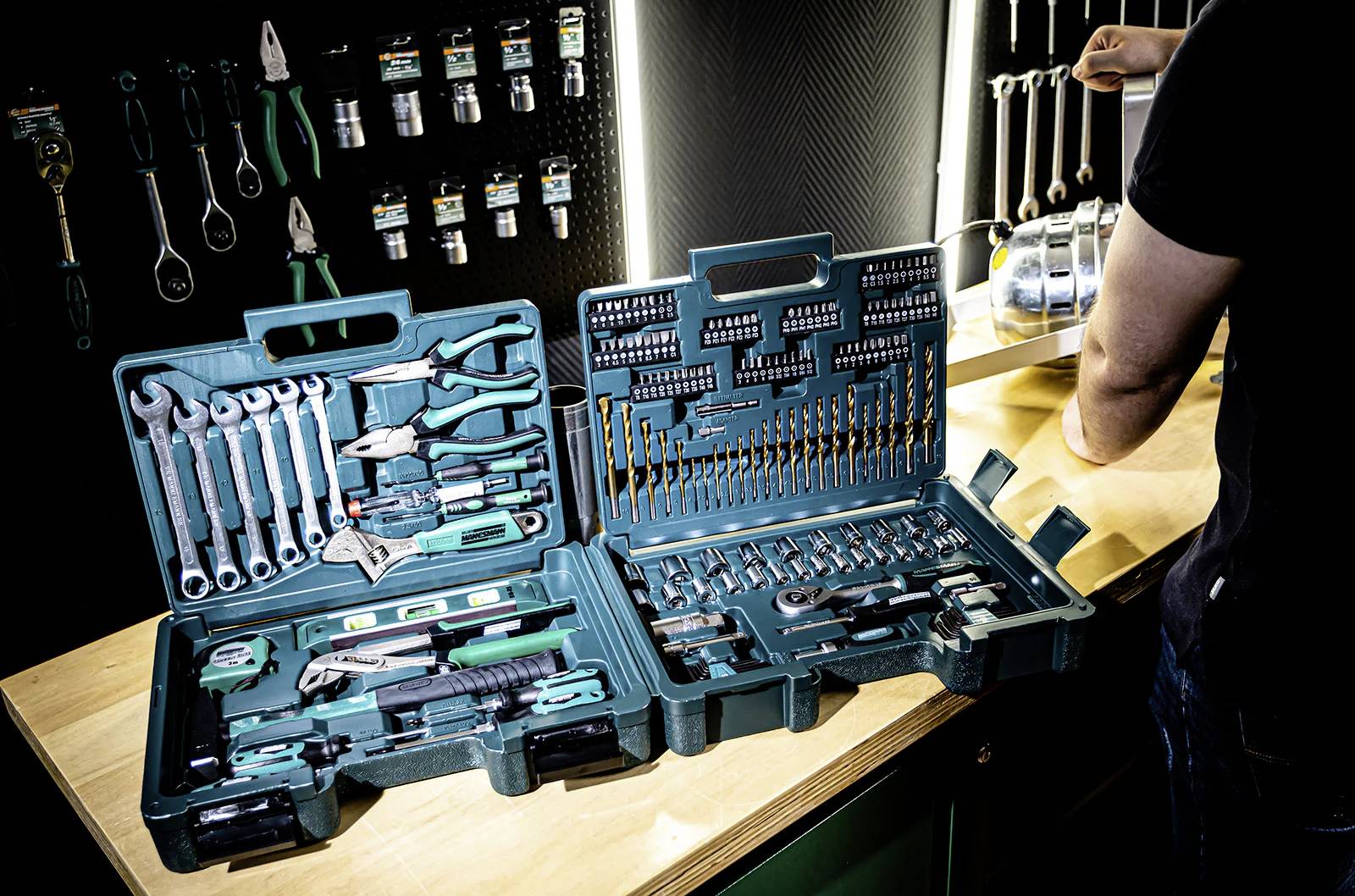 Un kit di attrezzi con vari strumenti tra cui chiavi, punte da trapano e pinze, esposto aperto su un banco da lavoro in un ambiente di officina.