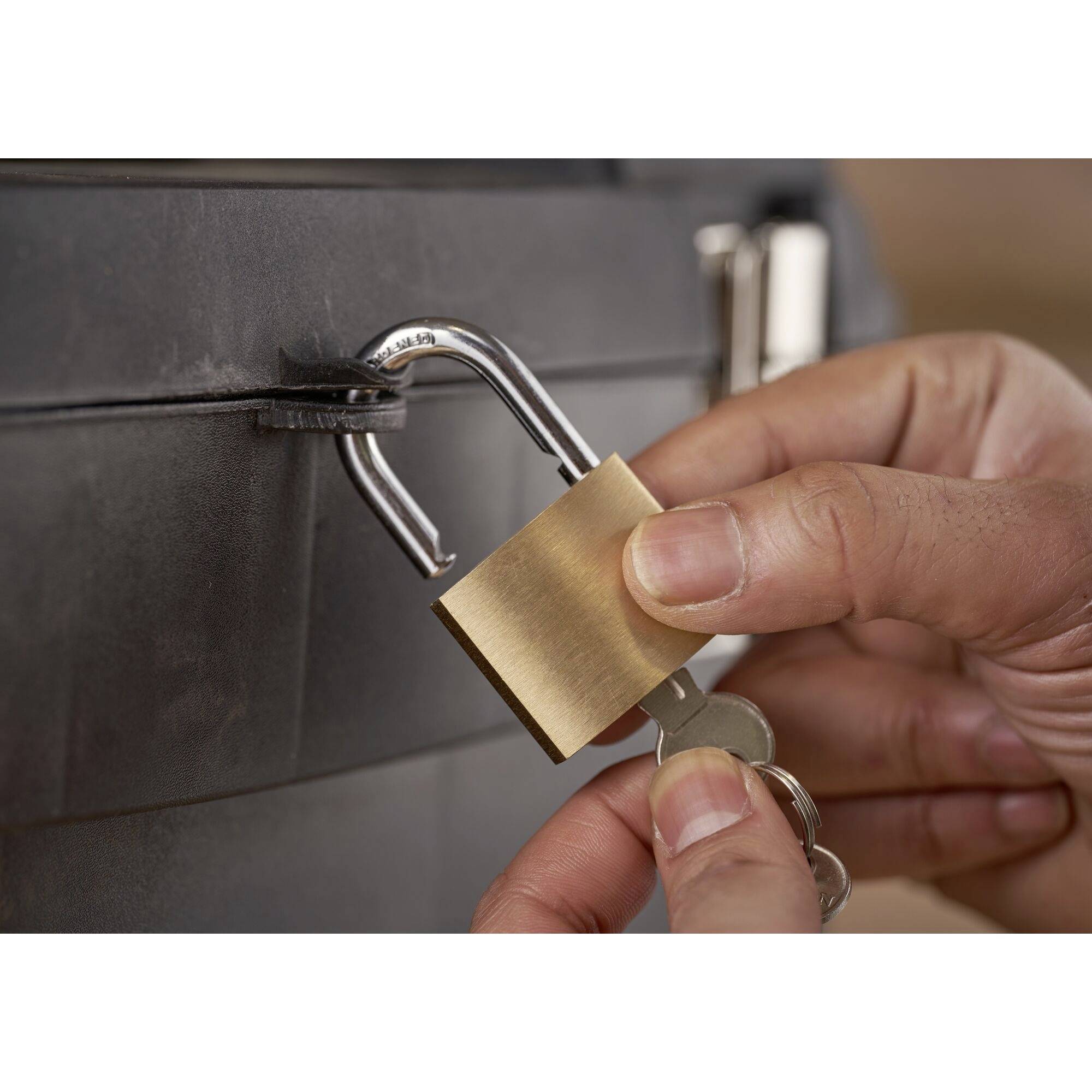 Una mano inserisce una chiave in un lucchetto fissato a una scatola nera di metallo.