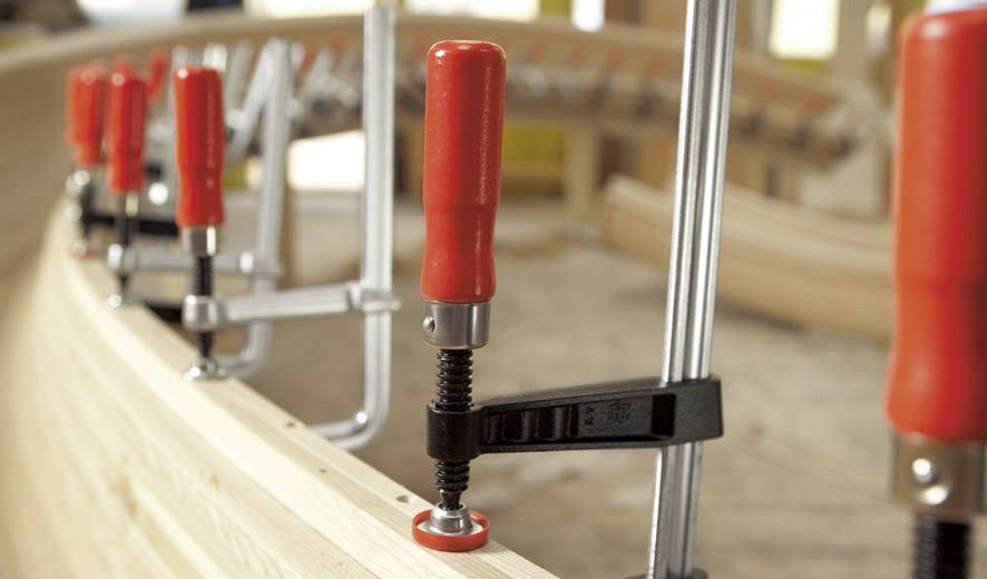 Diverse morse rosse tengono insieme parti di legno in un laboratorio. Focus sul lavoro artigianale e sulla costruzione.