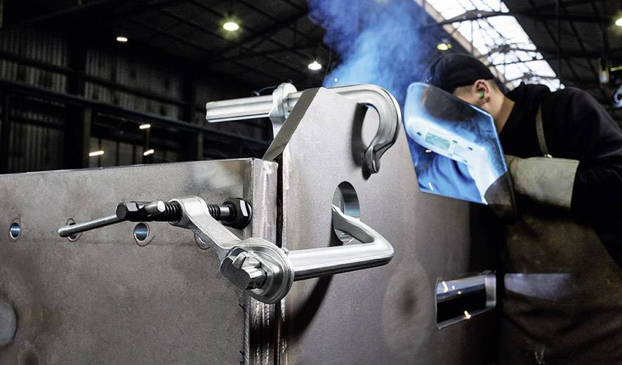 Un saldatore lavora con concentrazione su un grande pezzo di metallo in un capannone industriale. Scintille volano mentre indossa i dispositivi di protezione individuale.