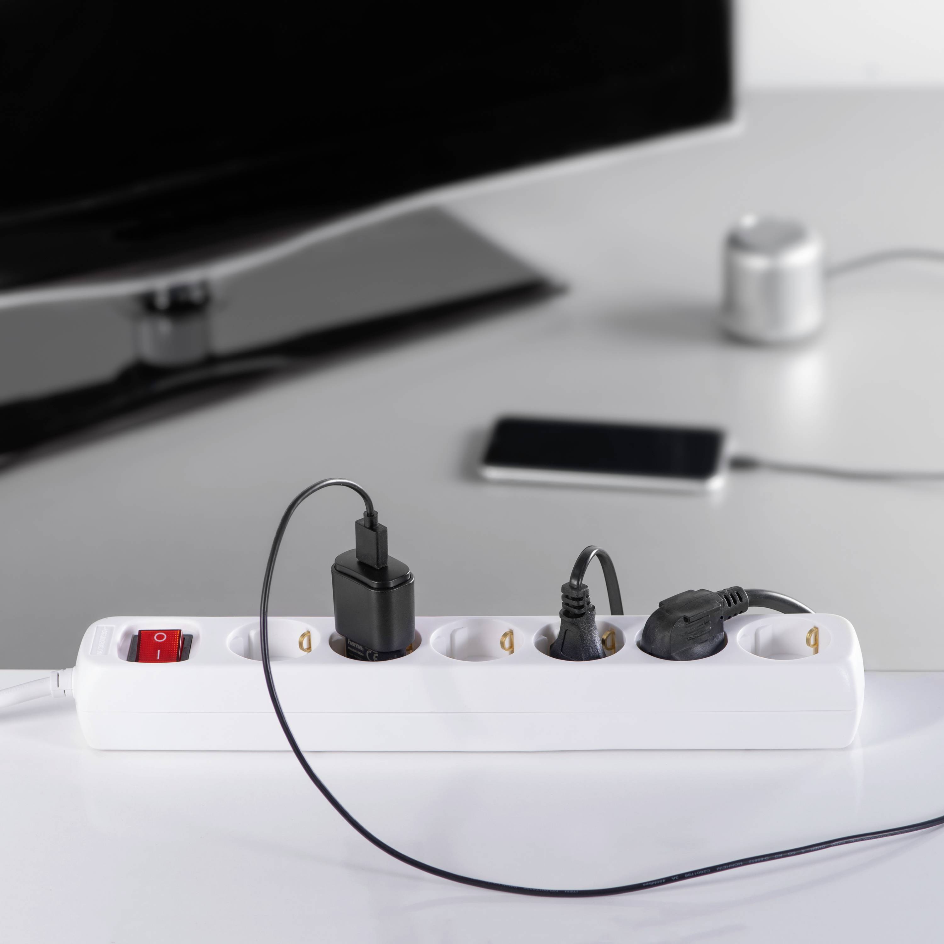 Una multipresa bianca su un tavolo con diversi dispositivi, tra cui un cavo di ricarica per uno smartphone.