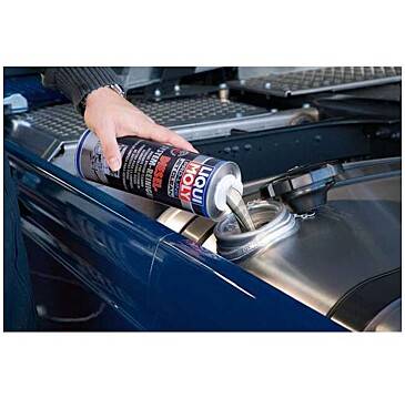 Additivo per carburante 'Liqui Moly' versato nel serbatoio del carburante di un'auto. Mano che tiene la bottiglia sopra il tappo del carburante aperto del veicolo.