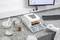 Un posto di lavoro in laboratorio con uno strumento per la misurazione dell'umidità, circondato da contenitori per campioni e uno schermo del computer che mostra dei dati.