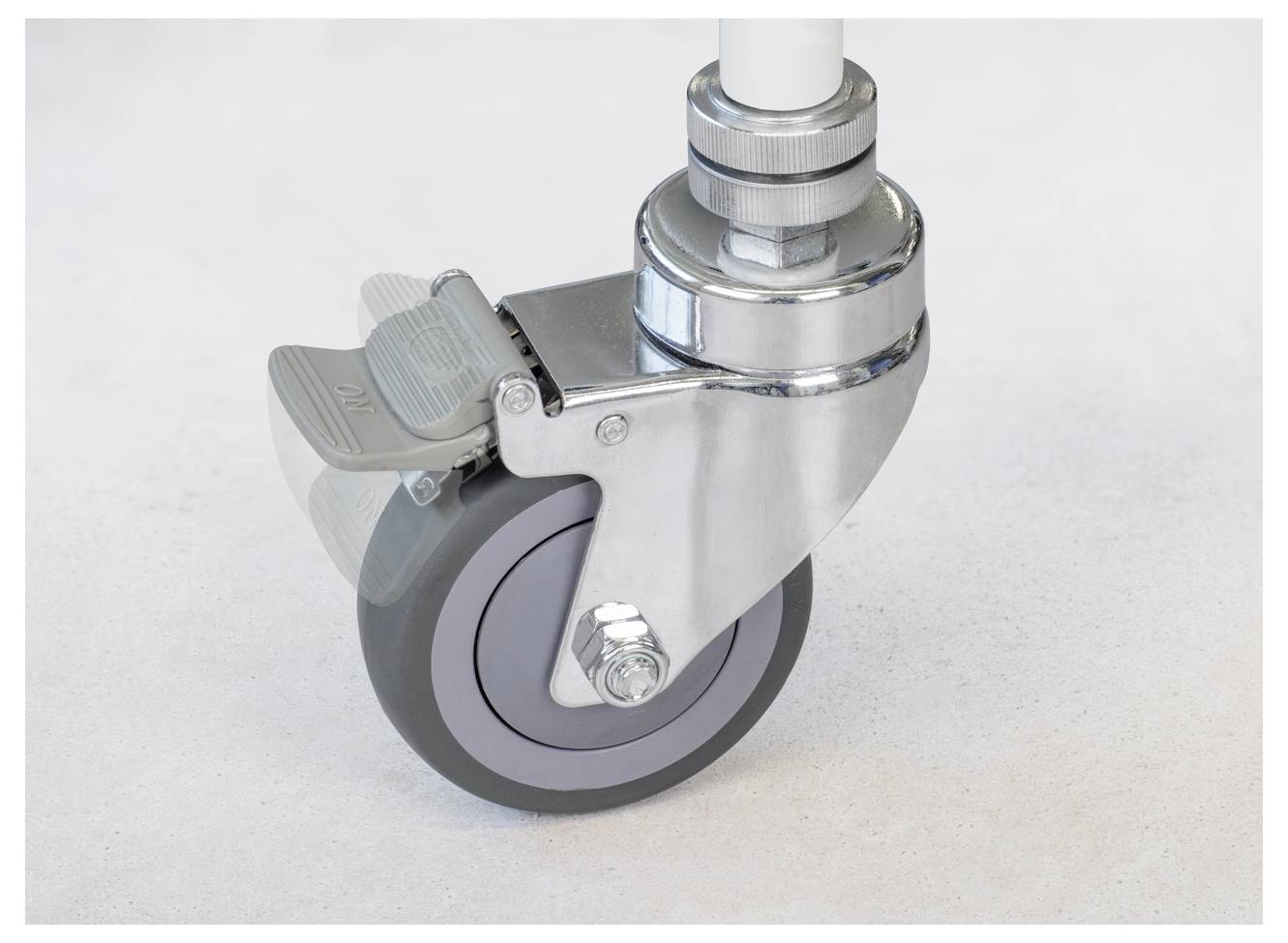 Ruota metallica per mobili con battistrada in gomma grigia, giunto girevole e freno di bloccaggio su superficie chiara. Adatta per carichi pesanti e movimentazione fluida.