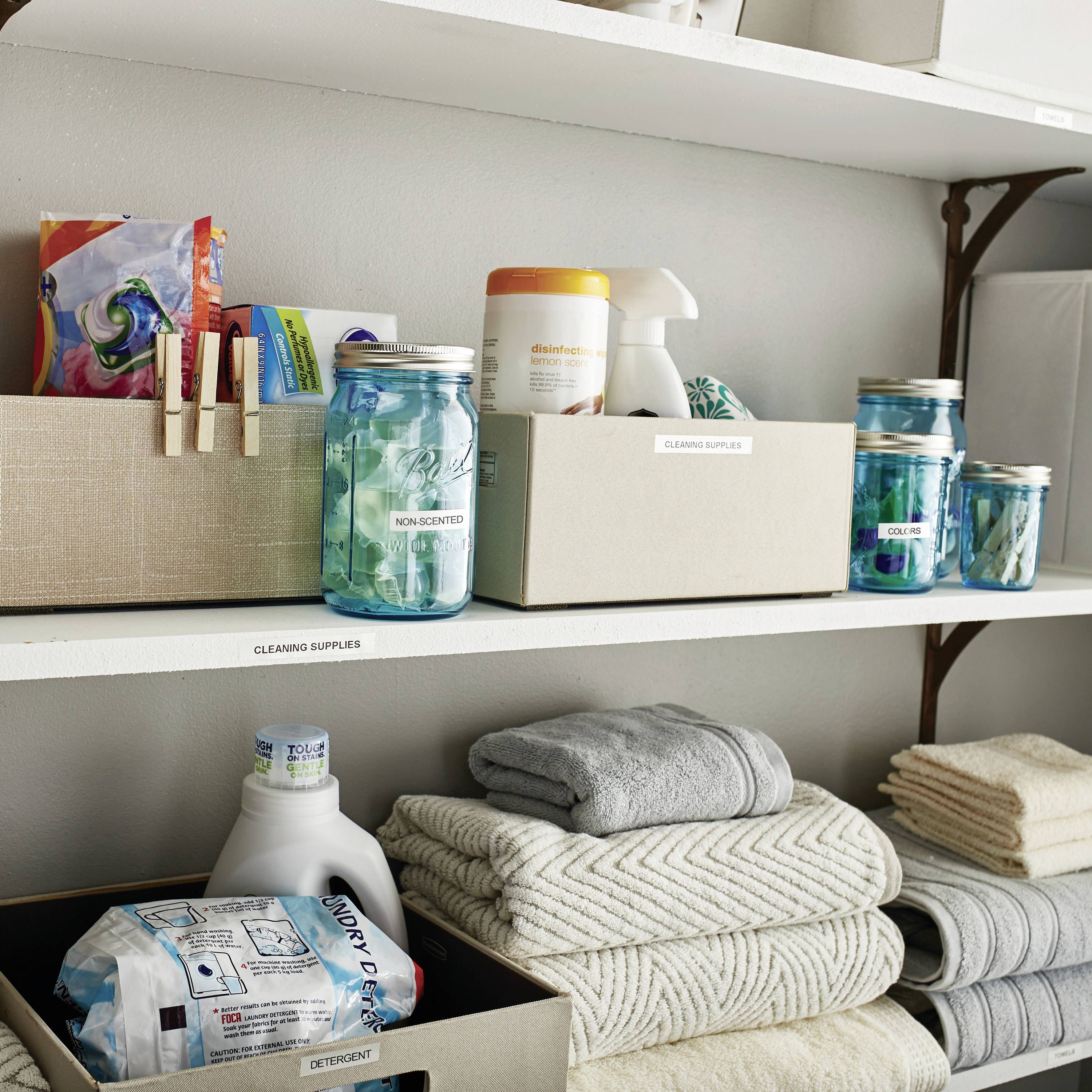 Soluzioni di stoccaggio per bagno con detergenti, asciugamani e bicchieri. Ordinatamente disposte e con etichette.