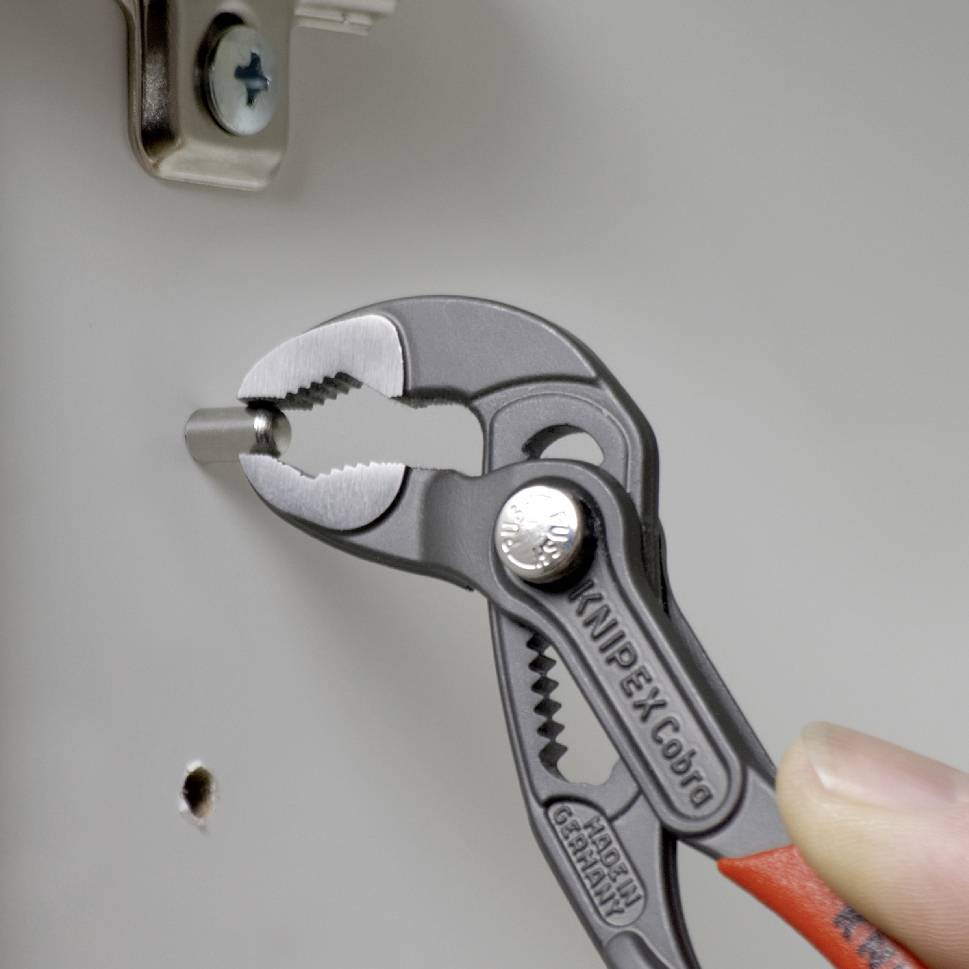 Una mano tiene una pinza per pompa idraulica che serra una vite su un pezzo di metallo. La pinza è del marchio KNIPEX Cobra.