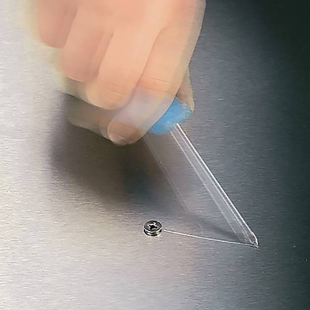 Una mano tiene un utensile di plastica, rimuovendo il film protettivo dalla superficie di un lamierino. Una vite è visibile sul bordo del metallo.