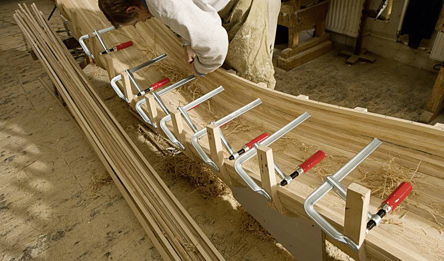 Una persona sta lavorando in un laboratorio a un progetto in legno, utilizzando grandi morsetti per mantenere i pezzi di legno in posizione.