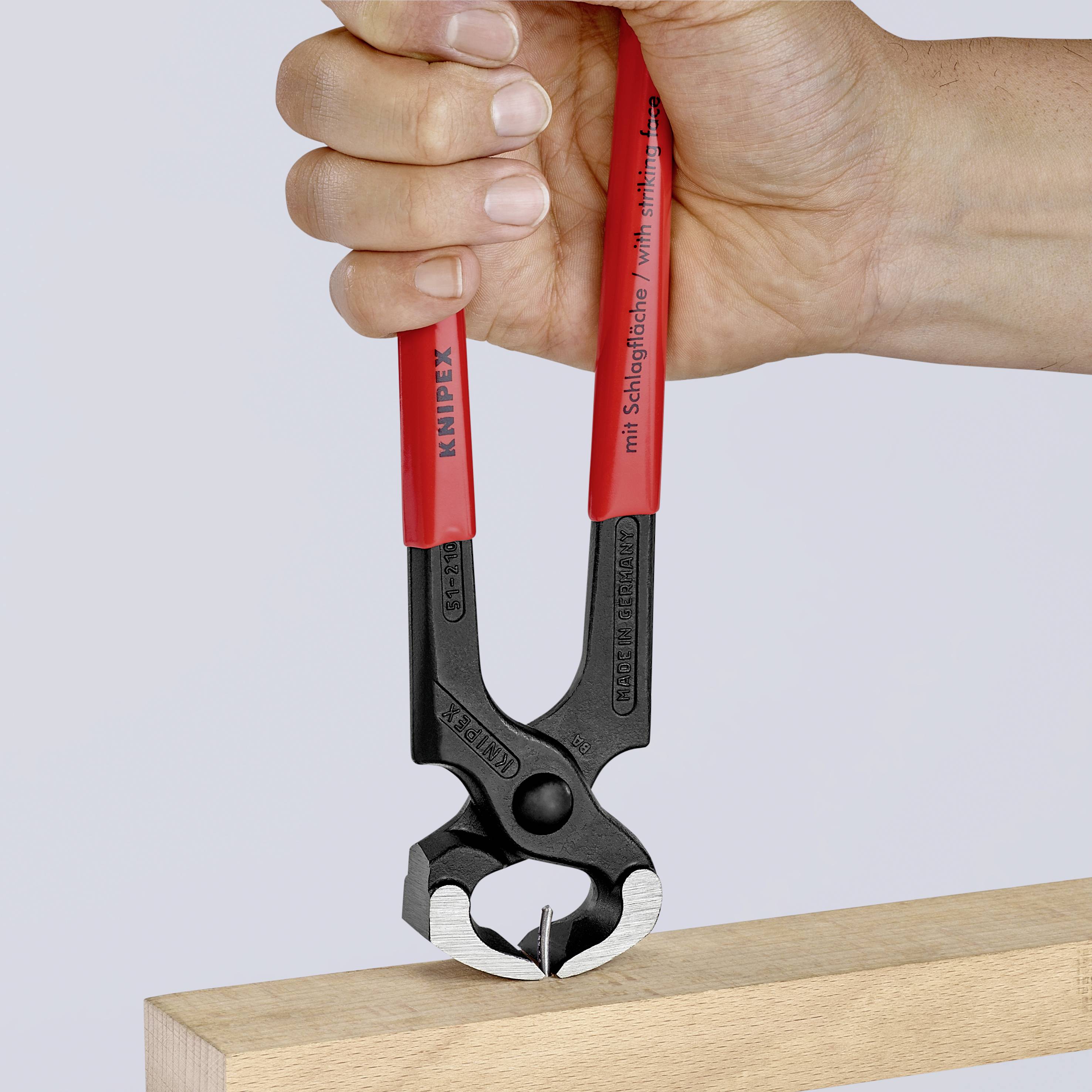 Una mano tiene una pinza rossa Knipex, premendola su un taglio per chiodi in un pezzo di legno.