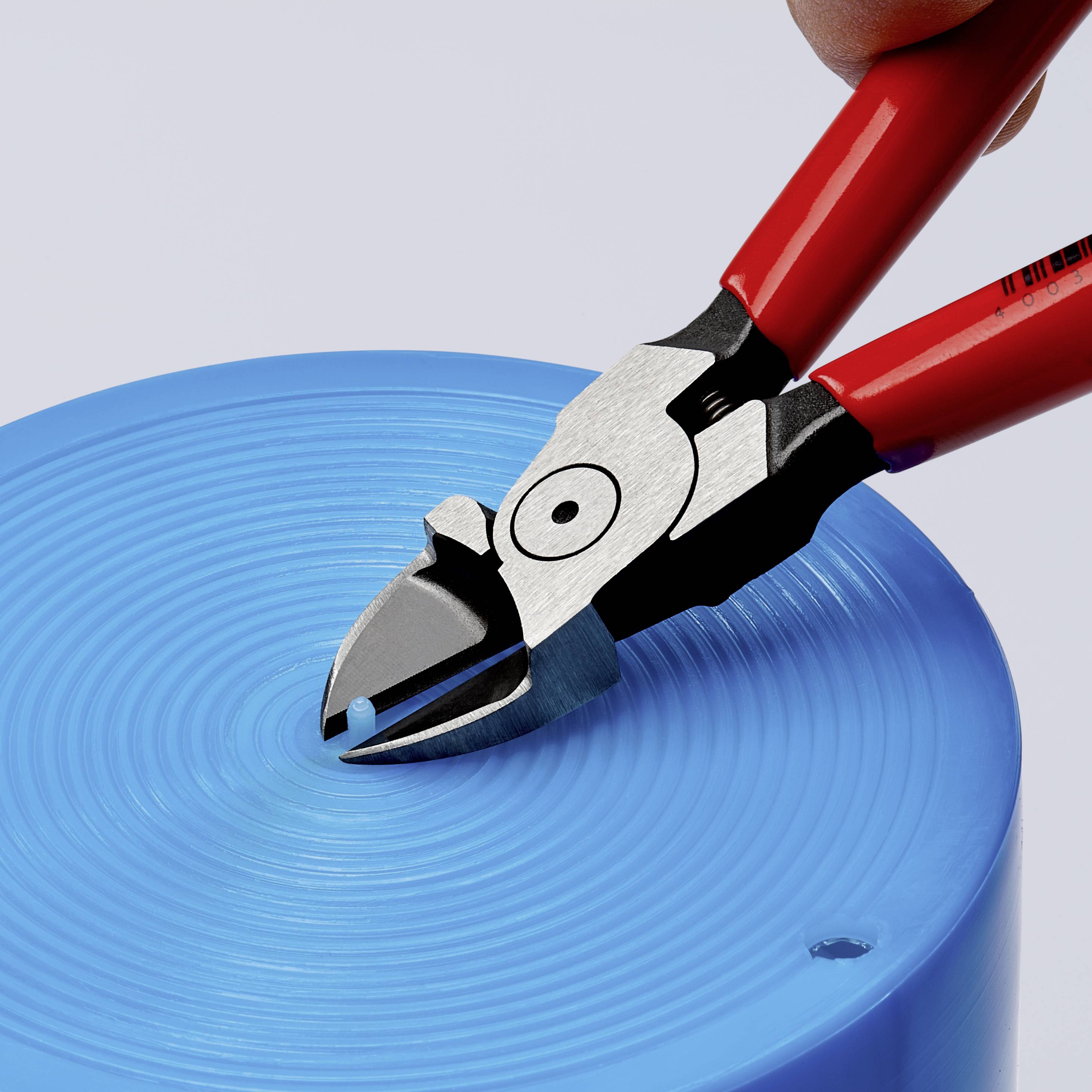 Una pinza rossa taglia un oggetto in plastica blu. L'azione mostra la funzione della pinza nel taglio di materiali duri.