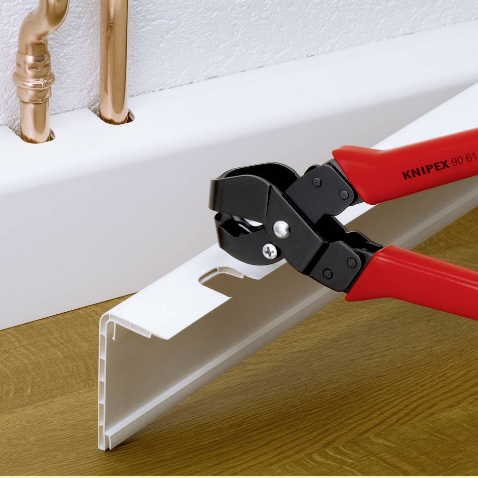 Viene mostrato un utensile per tagliare tubi di plastica. Viene posizionato su un tubo bianco. Tubi di rame sono visibili sullo sfondo.