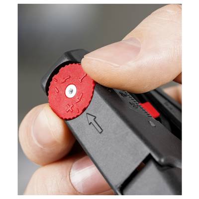Un dito di una persona ruota una manopola rossa in plastica con simboli di più e meno, fissata a un dispositivo nero, indicando tensione o calibrazione.