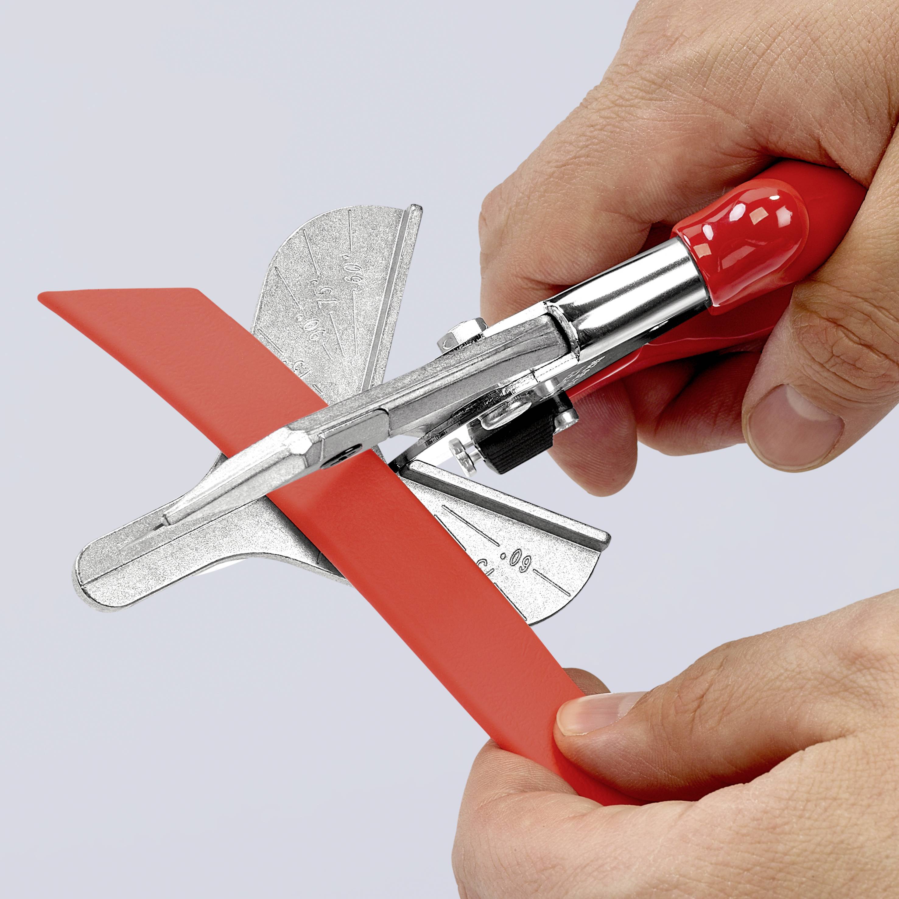 Una mano utilizza un attrezzo da taglio manuale rosso per tagliare un pezzo di plastica rossa.