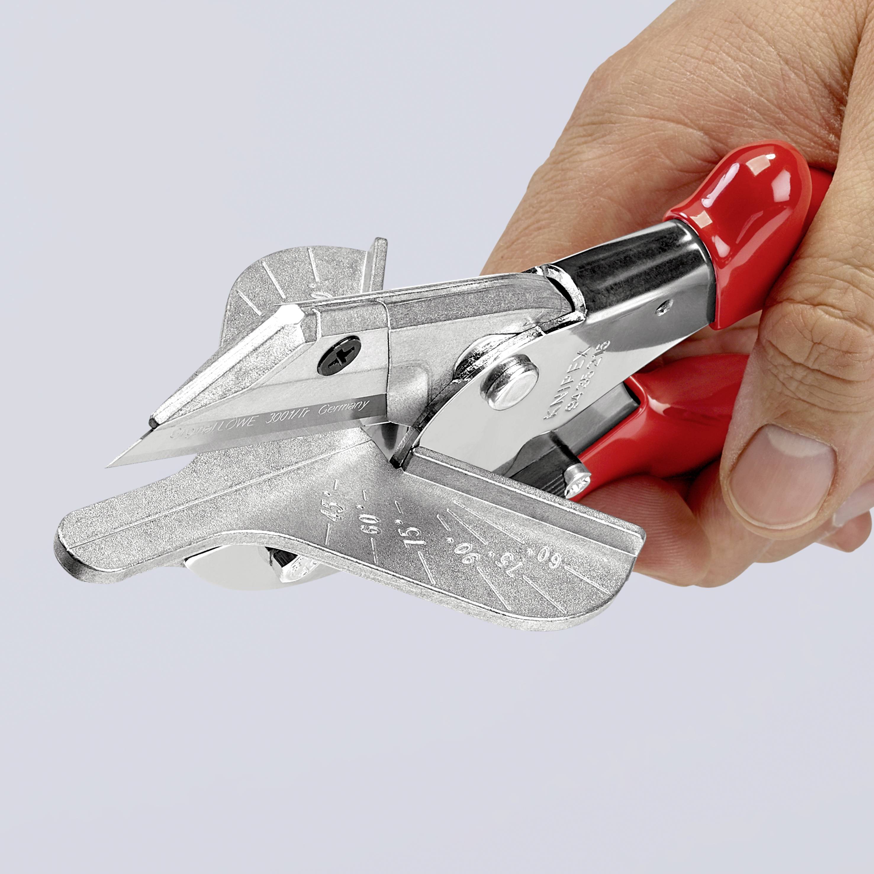 Una forbice rossa con lame metalliche viene tenuta da una mano, aperta e utilizzata per tagliare una sottile striscia metallica.