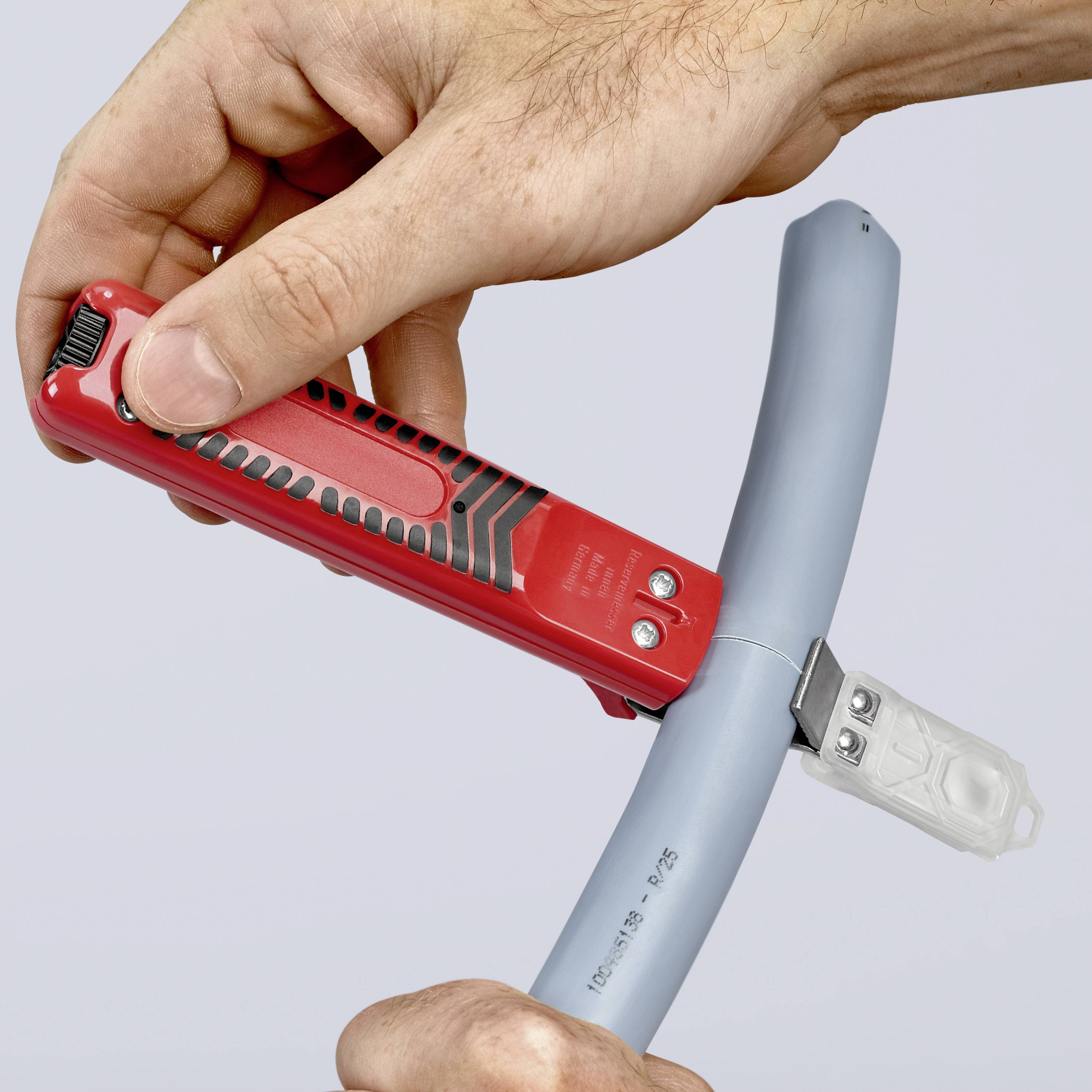 Una mano utilizza un utensile rosso per la spellatura per tagliare e spellare un cavo grigio.