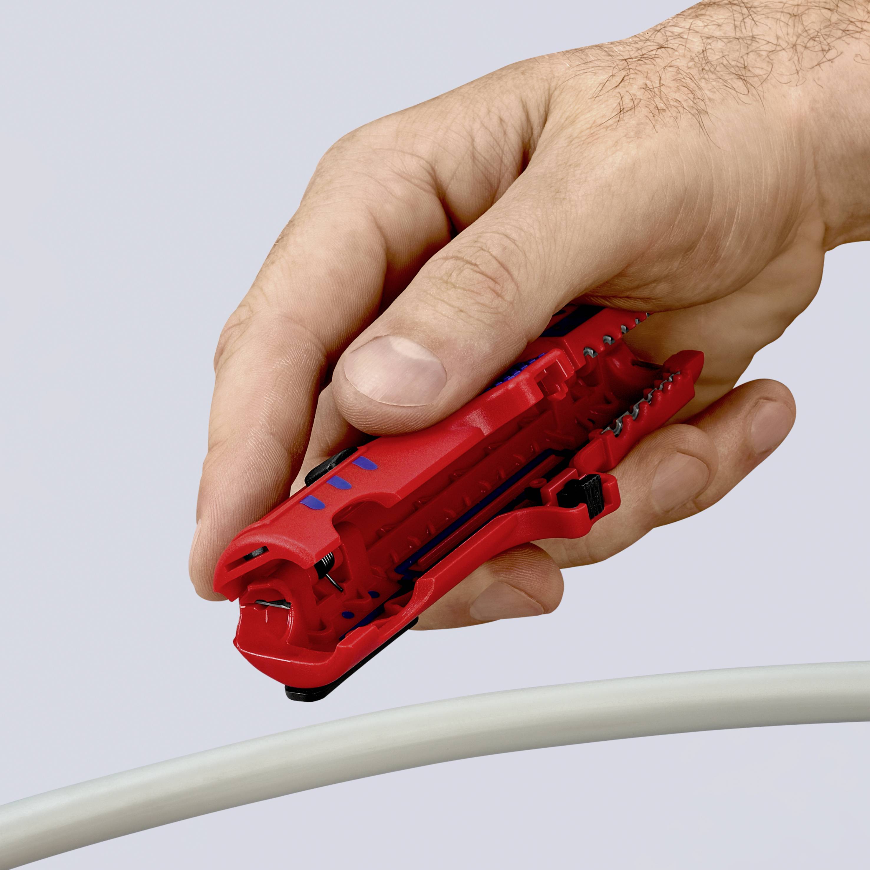 Una mano sta utilizzando un utensile rosso per tagliare cavi, intento a tagliare un cavo bianco.