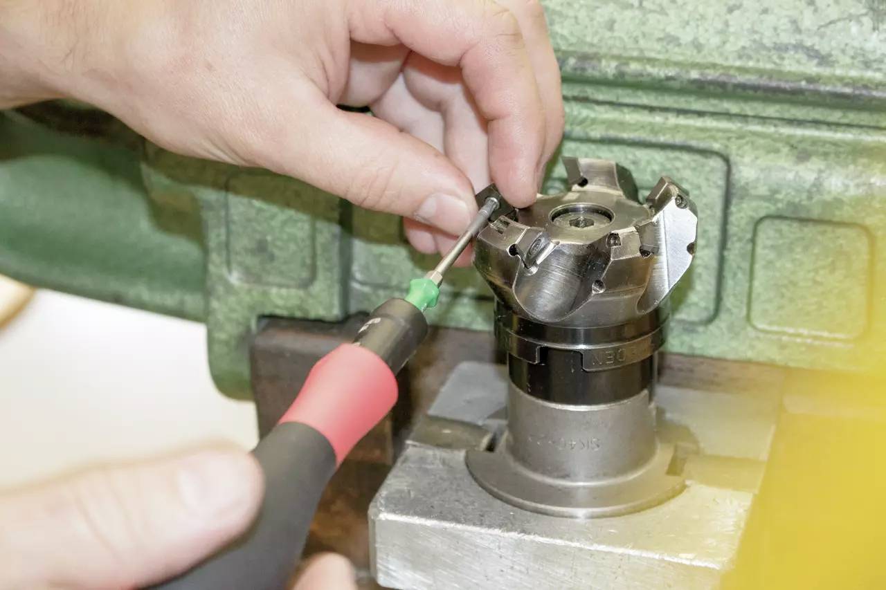 Primo piano di mani che lavorano con un cacciavite su un utensile da fresatura fissato in una macchina.