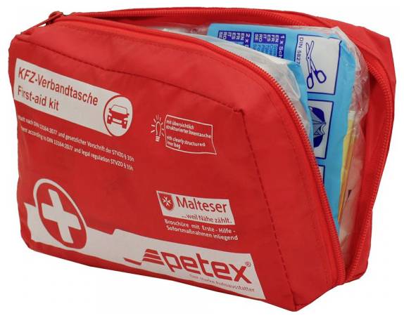 Un kit di pronto soccorso rosso con un simbolo a croce, etichettato 'KFZ-Verbandtasche First-aid kit.' È parzialmente aperto, che rivela forbici e forniture.