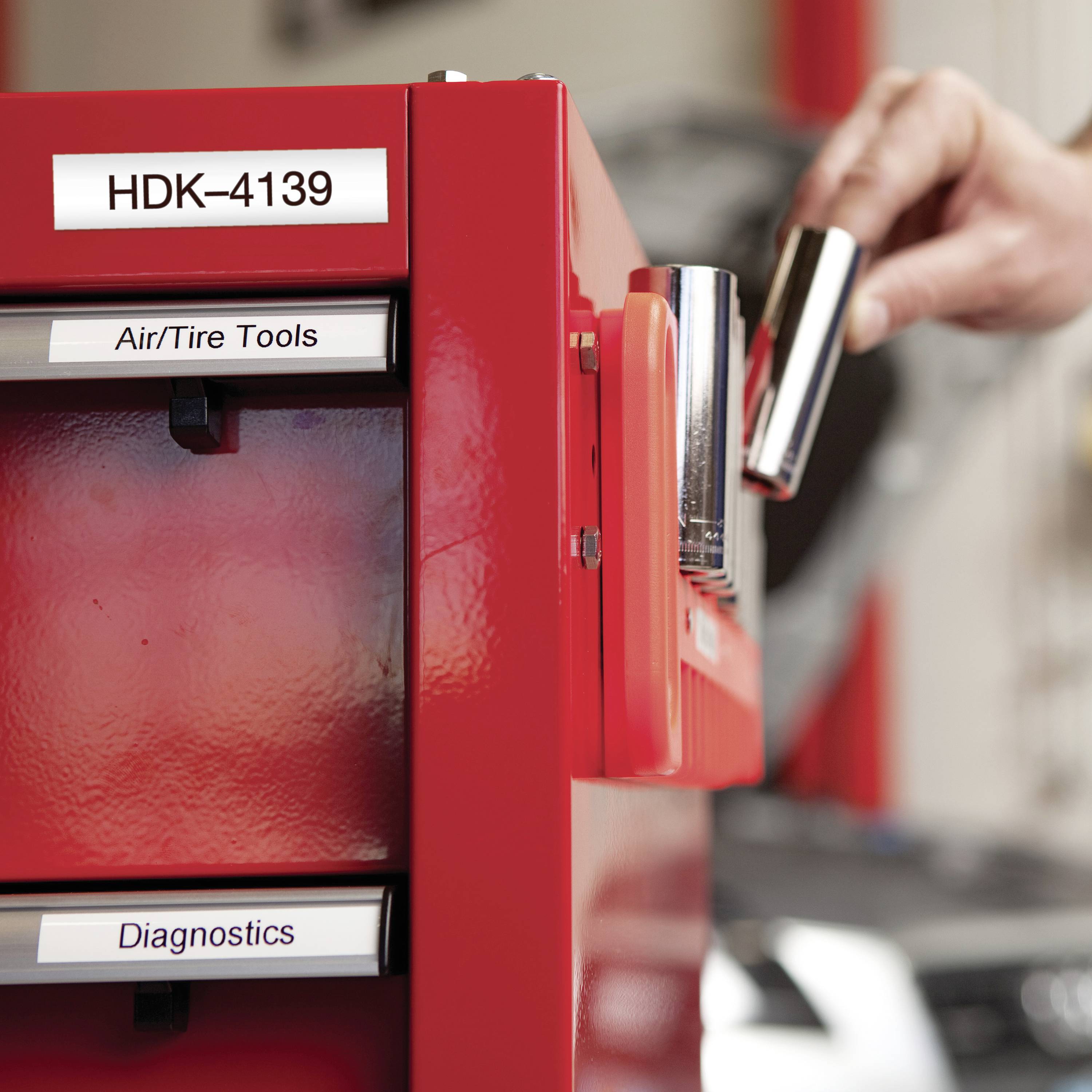 Una persona sta prelevando un attrezzo da un armadietto rosso con le etichette 'Attrezzi per Aria/Pneumatici' e 'Diagnostica'.