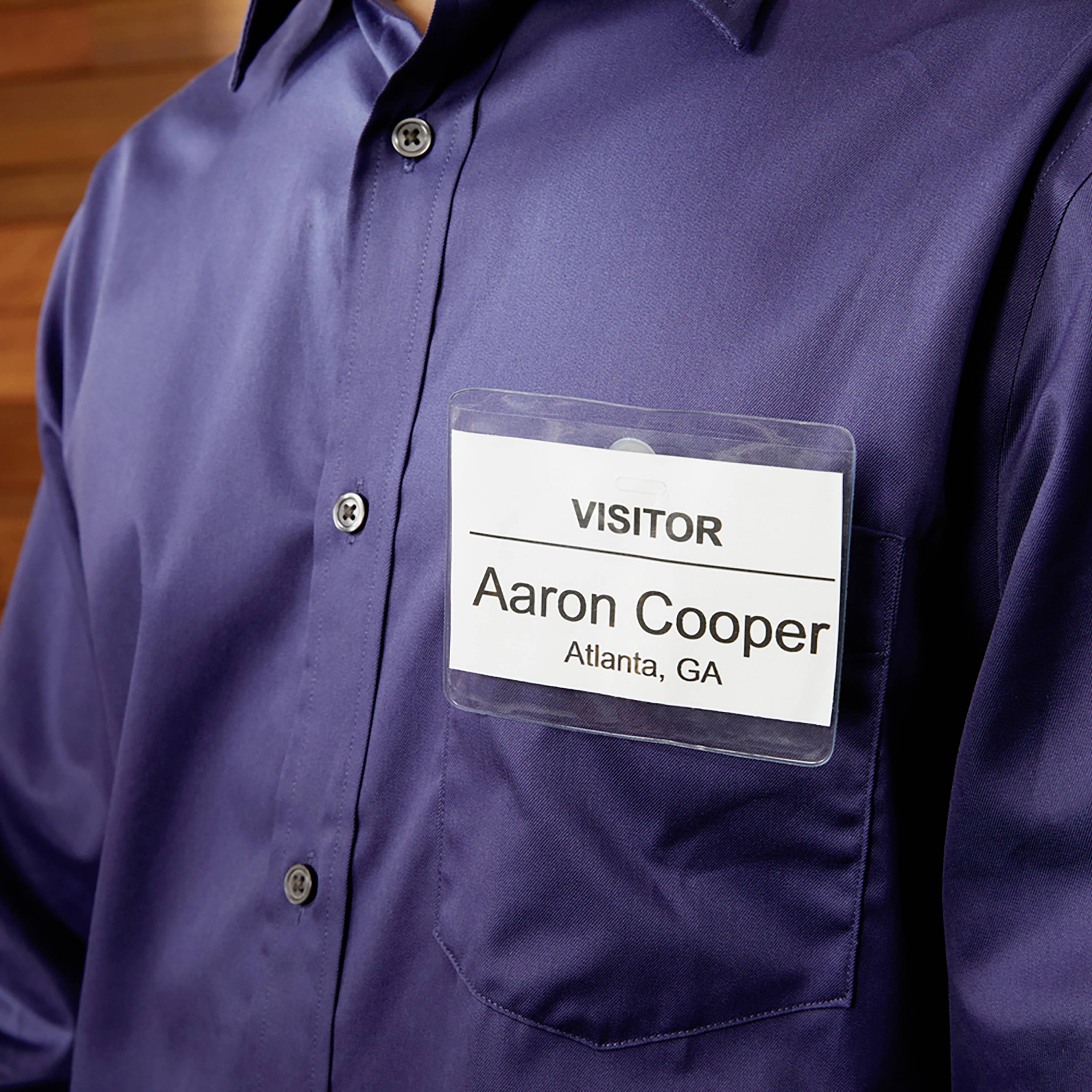 Persona con camicia blu scuro indossa un cartellino identificativo con la scritta 'VISITOR', sotto il quale si legge 'Aaron Cooper, Atlanta, GA'.