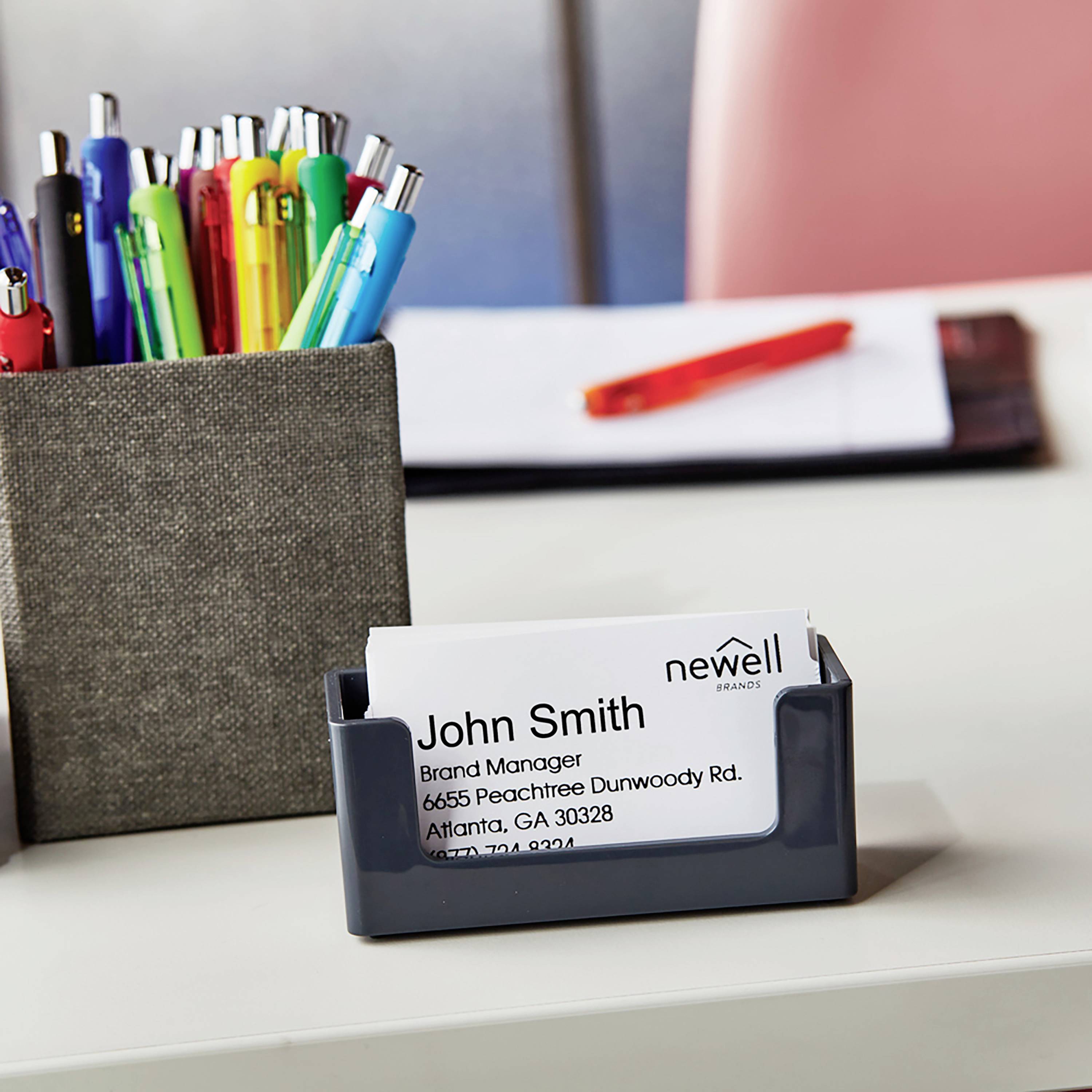 Portabiglietti da visita con un biglietto del marchio 'newell'. Il nome e le informazioni di contatto appartengono a un Brand Manager. Sullo sfondo, penne e appunti.