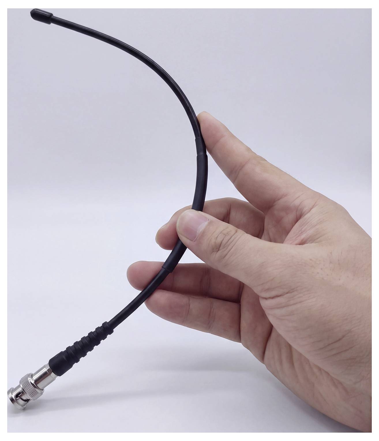 Una mano che tiene un cavo coassiale nero con un connettore metallico, mostrato su uno sfondo bianco neutro.