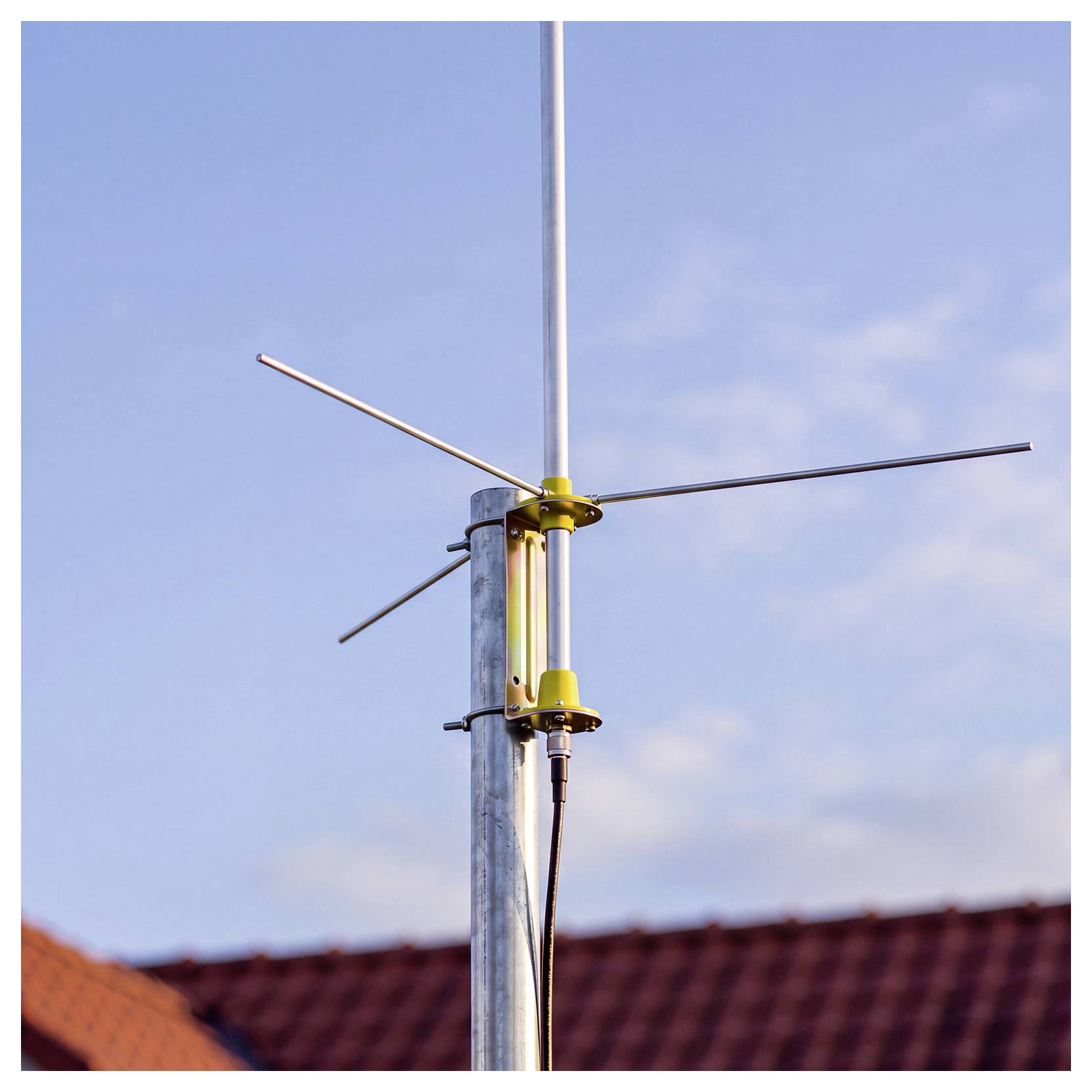 Un'antenna metallica montata su un palo contro un cielo blu, con tetti visibili sotto.