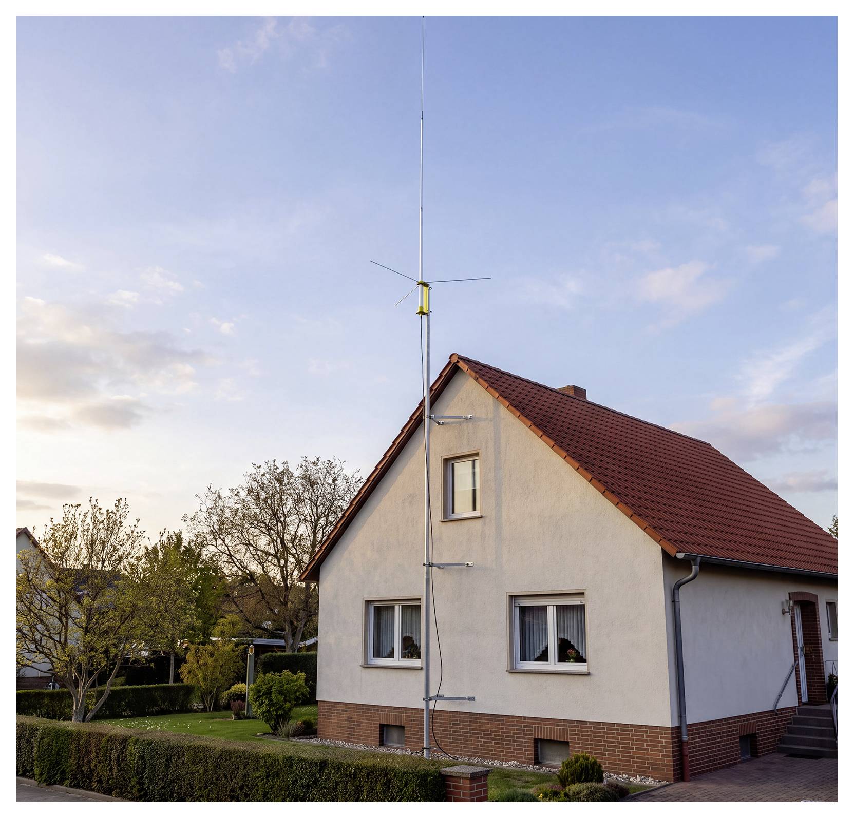 Una casa con una alta antenna sul tetto o un palo che si estende al di sopra del tetto contro un cielo sereno e luminoso al tramonto.