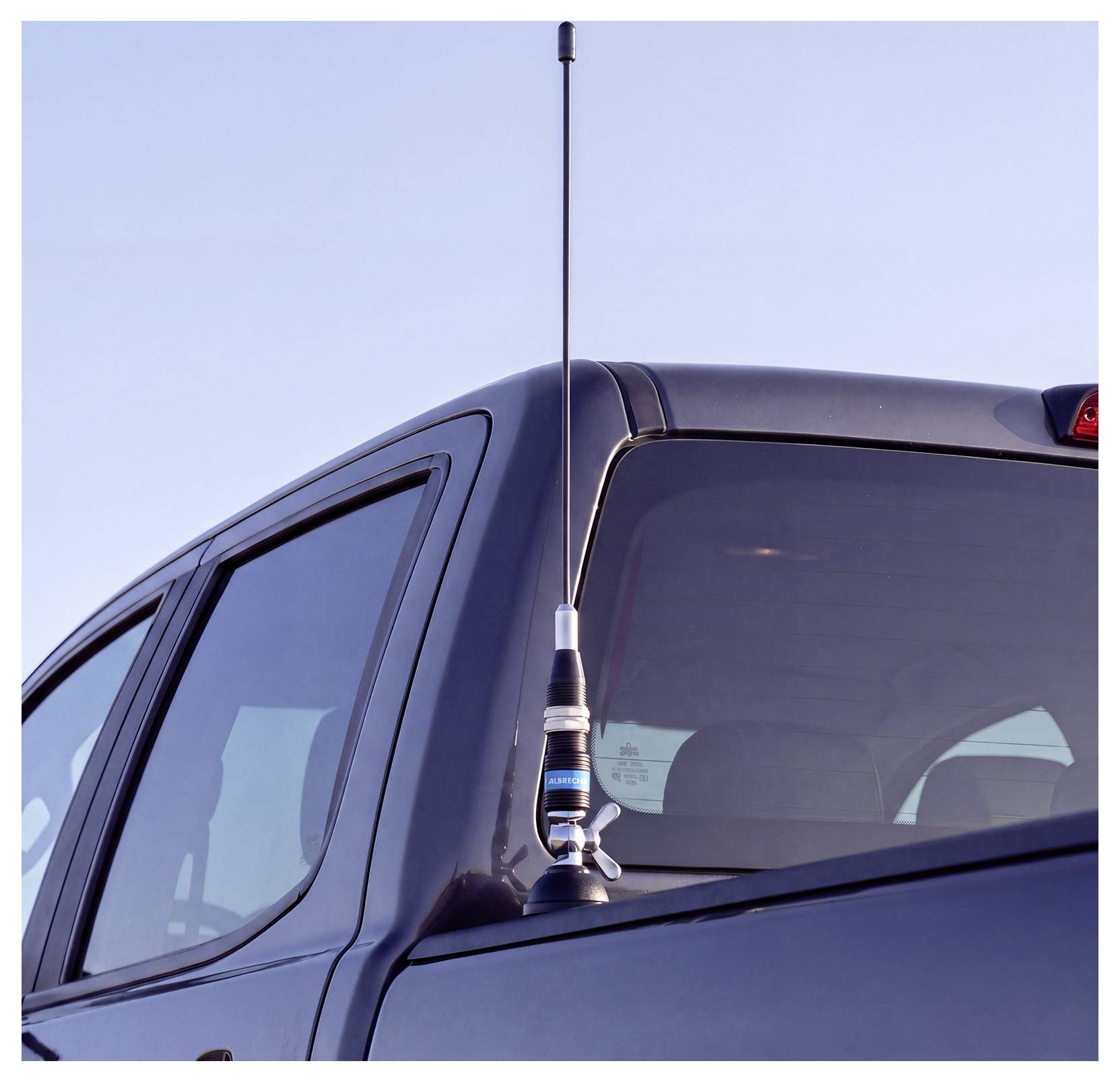 Antenna alta montata sul tetto di un pickup scuro contro un cielo limpido.
