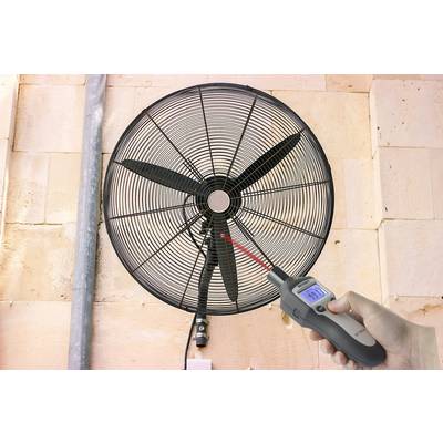 Una persona misura la velocità del vento di un grande ventilatore con un anemometro digitale su una parete.