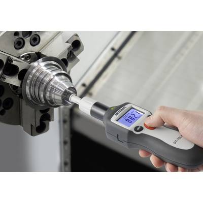 Una mano tiene un dispositivo di misurazione e verifica lo spostamento assiale di un pezzo metallico fissato in una macchina.
