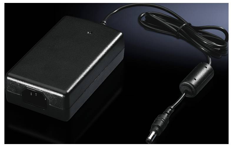 Un alimentatore nero con cavo e spina su sfondo scuro, utilizzato per l'alimentazione di dispositivi elettronici.