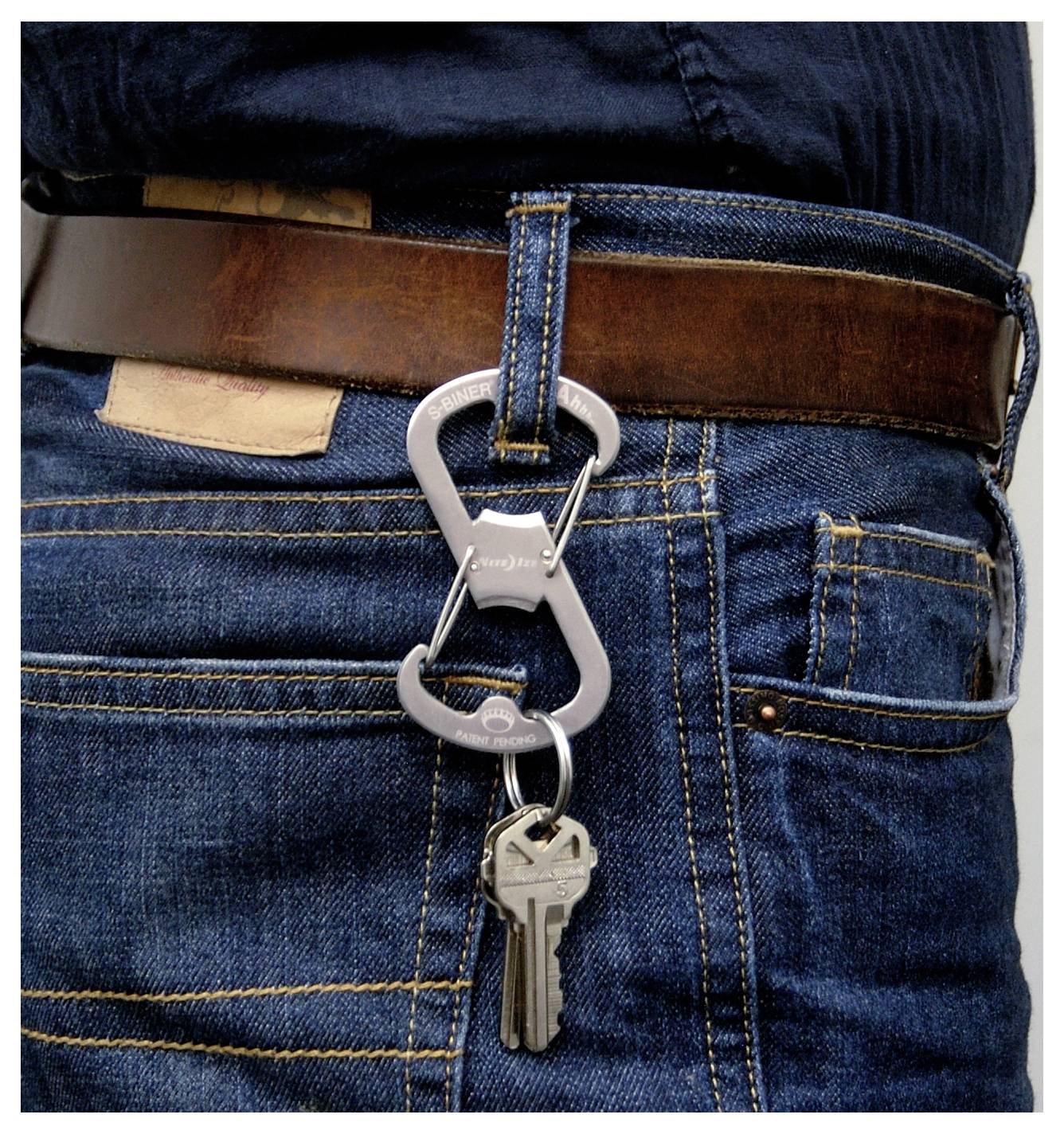 Un paio di chiavi argentate pende da un passante dei jeans blu, fissate con un moschettone metallico.