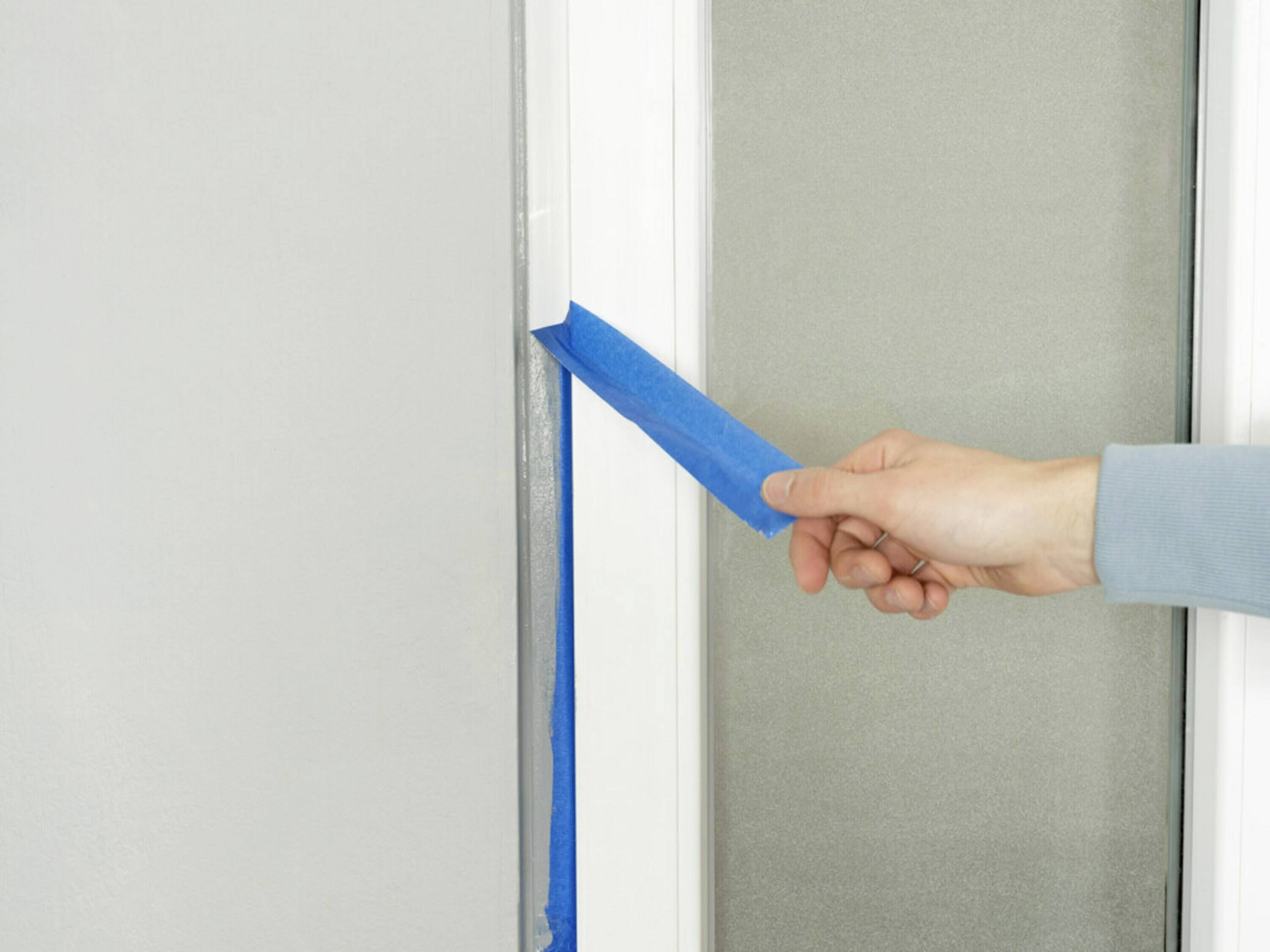Una mano sta staccando del nastro adesivo da un telaio della finestra, probabilmente dopo aver verniciato.